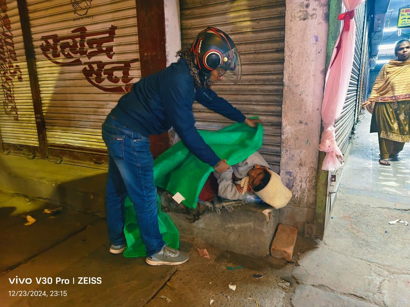 A KCCSRS volunteer covering a person sleeping on the street with a warm blanket at night